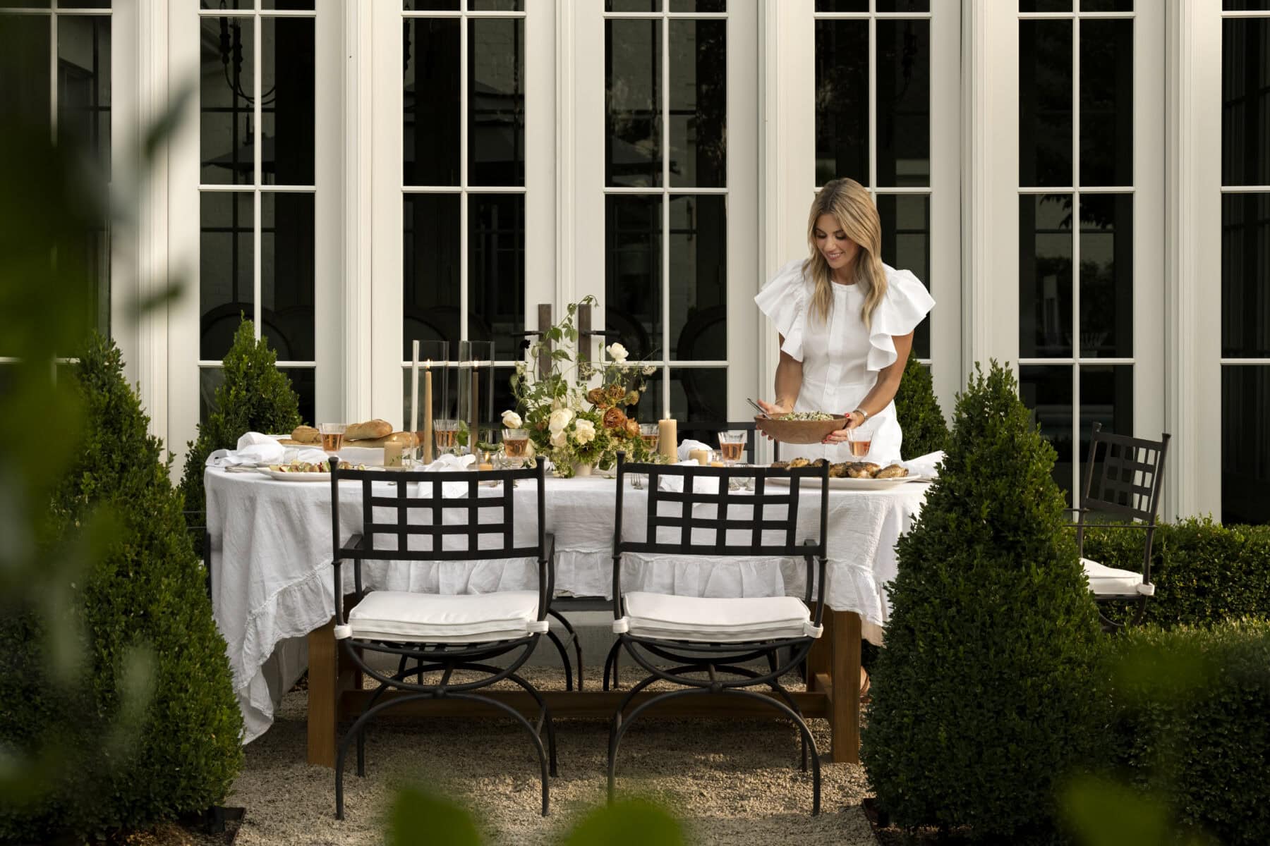 Shea McGee places a bowl of salad outside at a set dining table on a patio.
